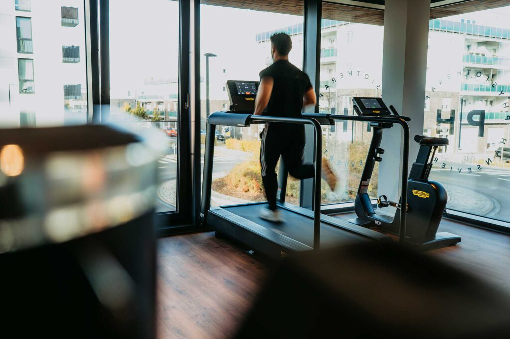 Ein Patient der läuft auf einem Laufband Physiotherapie Hanseviertel mit Blick auf das Lüneburger Hanseviertel.